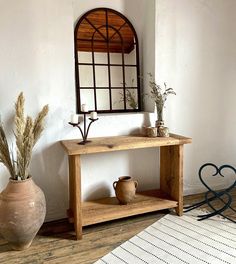 a wooden table sitting in front of a mirror on top of a white wall next to a potted plant