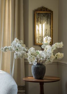 a vase filled with white flowers sitting on top of a table next to a mirror