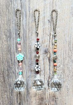 three necklaces are hanging from chains on a wooden surface with beads and charms attached to them