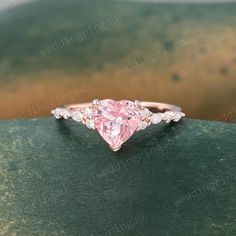 a pink heart shaped diamond ring on top of a green surface with water in the background