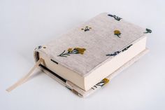 an open book with yellow flowers on it sitting on a white tablecloth covered surface