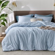 a bed with blue sheets and pillows in a room next to a potted plant