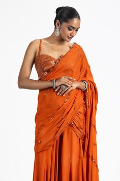 Rust orange pre-draped saree in georgette base with tonal resham and floral mirror embroidery. Paired with strap slevees mirror embroidered sweetheart neck blouse.
Components: 2
Pattern: Embroidery
Type Of Work: Tonal Resham and Mirror Work
Neckline: Sweetheart Neck
Sleeve Type: Sweetheart Neck
Fabric: Georgette
Color: Orange
Other Details: 
Floral mirror work tassels on saree hem
Occasion: Sangeet, Mehendi and Haldi - Aza Fashions Rust Saree, Sweetheart Neck Blouse, Draped Saree, Mirror Embroidery, Floral Mirror, Orange Saree, Drape Saree, Pattern Embroidery, Blouse For Women