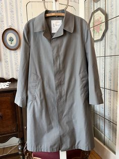 This classic overcoat is from London Fog, made from 65 per cent polyester and 35 per cent cotton in medium grey. It fastens with the original buttons in the front and has two front pockets, and it's fully lined with a beige, grey and black checked lining. Marked size 42 short. The measurements, taken with the coat lying flat, are: shoulder to shoulder, 19 inches; armpit to armpit, 22 inches; sleeves, 24 inches; length, 42 inches; bottom edge, 32 inches. In very good condition. Winter Gray Raincoat With Pockets, Classic Solid Raincoat With Pockets, Classic Long Single Breasted Raincoat, Gray Long Sleeve Outerwear For Rainy Weather, Classic Long Single-breasted Raincoat, Classic Long Winter Raincoat, Classic Long Sleeve Raincoat, Classic Long Raincoat, Gray Cotton Business Outerwear