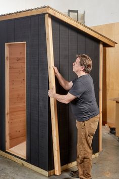 a man standing in front of a black shed with wood trimming on the side