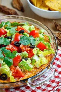 a salad with lettuce, tomatoes and black olives in a glass bowl