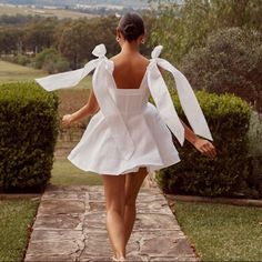 a woman in a white dress walking down a path