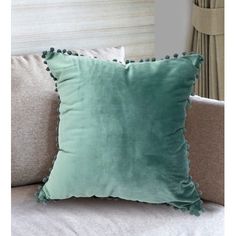 a green pillow with pom - poms on the back of it sitting on a couch