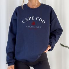 Elevate your seaside style with our Navy Crewneck Cape Cod Sailing Club Sweatshirt. Designed in a deep navy hue reminiscent of the Atlantic, it's the perfect companion for breezy days by the harbor or cozy evenings around a beach bonfire. Whether you're strolling along the picturesque Cape Cod coastline or enjoying a leisurely sail, this sweatshirt, adorned with the club emblem, embodies the maritime charm of the region. Crafted for both comfort and durability, it's equally suited for a day of adventure on the water or simply lounging at your favorite coastal cafe. Join the ranks of coastal enthusiasts and embrace the allure of Cape Cod with our signature sweatshirt. Navy Long Sleeve Marine Top, Navy Sailor Crew Neck Top, Marine Style Cotton Crew Neck Top, Nautical Cotton Crew Neck Top, Cotton Nautical Crew Neck Tops, Navy Relaxed Fit Crew Sweater, Navy Crew Neck Top With Letter Print, Nautical Cotton Crew Neck Sweater, Nautical Cotton Sweater With Crew Neck