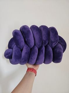 a hand holding up a purple pillow that is shaped like a caterpillar