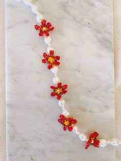 the beaded necklace has red and yellow flowers on it, along with pearl beads