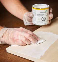 a person in white gloves painting a piece of wood with a paint can next to it