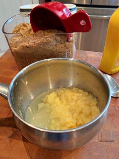 a metal bowl filled with food on top of a wooden table next to a measuring cup