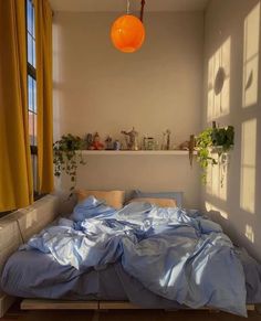 an unmade bed in a small room with yellow curtains and potted plants on the window sill