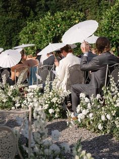 several people sitting in chairs with umbrellas over their heads and flowers on the ground