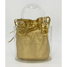 Vintage Salvatore Ferragamo Clear Bucket Bag with Gold Pouch in fair condition. Clear acrylic curved hardshell bucket with double handles and gold tone signature ferragamo hardware at each end of handles. Gold leather drawstring interior pouch can be easily removed from the clear bucket. The pouch is lined in beige nylon with a matching leather double pull drawstring style top. Overall fair vintage condition. The clear bucket does have scuffs and scratches consistent with age and use. the hardwa Elegant Bucket Bag With Brass Hardware, Elegant Top Handle Bucket Bag With Brass Hardware, Modern Gold Bucket Bag For Evening, Formal Gold Bucket Bag With Detachable Strap, Designer Gold Bucket Bag For Everyday Use, Modern Gold Bucket Bag For Formal Occasions, Modern Gold Evening Bucket Bag, Gold Rectangular Bucket Bag With Removable Pouch, Modern Gold Bucket Bag With Detachable Strap