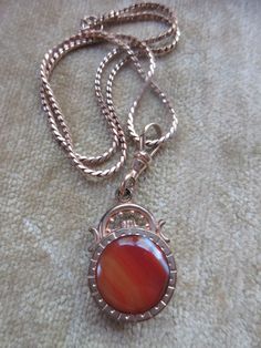 Antique agate watch fob necklace in gold fill. Our antique watch fob is adorned with a stone on each side. A carnelian colored banded agate on one side a a dark stone on the reverse make the double sided fob a striking piece. It suspends from a 16'' gold fill chain that closes with an old fashioned C thumb spring clasp. A swivel hook acts as the bail and brings the pendant to a length of one and seven eighths of an inch x .75''. The fob is older than the chain which may date to the 1930s. These pieces exhibit age appropriate wear with some scratching and finish loss. This estate found necklace will make an interesting layering necklace with your other antique pieces. Vintage Carnelian Jewelry With Polished Finish, Vintage Polished Carnelian Jewelry, Vintage Carnelian Engraved Jewelry, Antique Gemstone Jewelry For Memorial, Classic Carnelian Jewelry Hallmarked, Antique Cabochon Round Pendant Jewelry, Vintage Gemstone Jewelry For Memorial, Antique Engraved Carnelian Jewelry, Formal Agate Pendant Jewelry