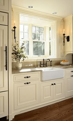 a kitchen with white cabinets and wood flooring next to a large window in the wall