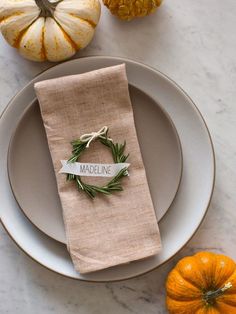 a place setting with napkins, pumpkins and greenery on the table in front of it