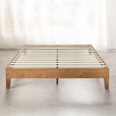 a wooden bed frame sitting on top of a white floor next to a curtained window