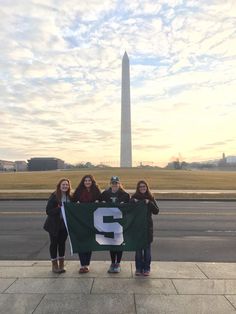 three girls holding up a green and white number two banner in front of the washington monument