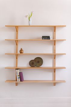 a wooden shelf with books and vases on the top, against a white wall