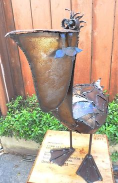 a metal vase sitting on top of a wooden table next to a fence and shrubbery