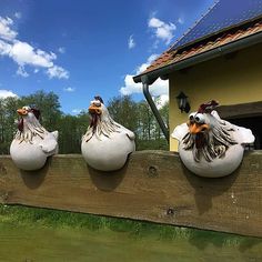 three ceramic chickens sitting on top of a wooden fence