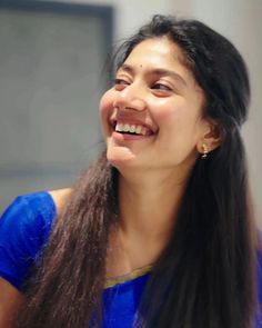 a woman with long hair smiling and holding a cell phone to her ear while wearing a blue shirt