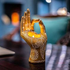 a small golden hand holding a candle on top of a table next to a laptop