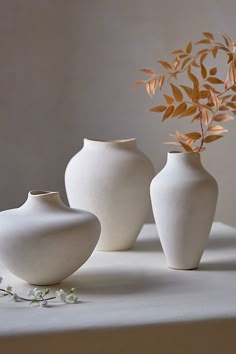 three white vases sitting on top of a table