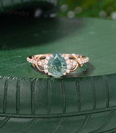 an oval shaped ring with a green stone surrounded by white diamonds on a green surface