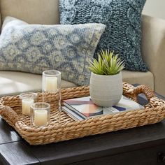 a wicker tray with candles on top of it in front of a couch and pillows