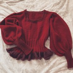 a red sweater with ruffles is laying on a white sheet and it's sleeves are open