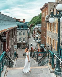 a woman in a white dress is walking down the stairs at an old town street