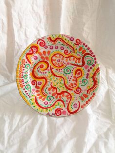 a colorful plate sitting on top of a white cloth covered tablecloth with an intricate design