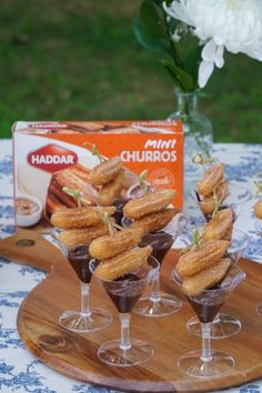 small desserts are arranged in wine glasses on a wooden tray next to a box of churros