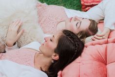 two women laying on a pink couch with a white dog in their lap looking at the camera