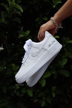 a person is holding up a white nike air force shoe in front of some bushes