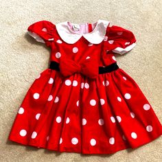 a red dress with white polka dots and a black bow on the front, sitting on carpet