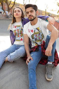 a man and woman sitting on top of a skateboard in front of some trees