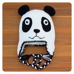 a crocheted panda bear hat on top of a wooden table next to a pair of scissors