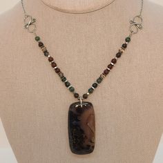 Made with love, this necklace features a stunning Stick Agate pendant stone flanked by Bronzite, Biotite, Mahogany Jasper, Smokey Quartz, and Hill Tribe Silver. At 22 3/4" long, this piece is sure to make a statement! Check out the coordinating earrings. Wire Wrapped Agate Dangle Jewelry, Brown Natural Stone Pendant Jewelry, Dangle Jasper Jewelry With Natural Stones, Wire Wrapped Agate Pendant Jewelry, Natural Stone Jasper Dangle Jewelry, Natural Jasper Stone Dangle Jewelry, Brown Dangle Jewelry With Natural Stones, Brown Natural Stone Dangle Earrings, Brown Dangle Earrings With Natural Stones