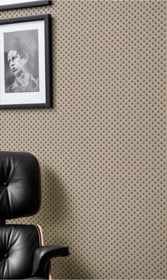 a black leather chair sitting in front of a wall with a framed photo on it