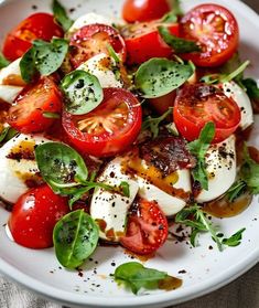 a white plate topped with sliced tomatoes and mozzarella on top of lettuce