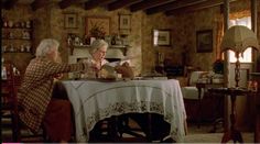 an older couple sitting at a table in a living room with the woman pouring tea