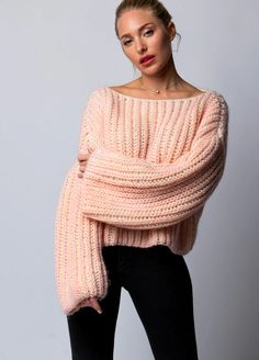 a woman is wearing a pink sweater and black pants with her hands on her hips