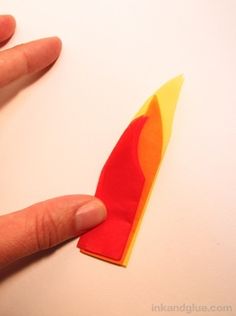 a hand is holding a piece of paper with an orange and red design on it