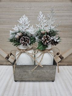 two mason jars with pine cones tied to them are sitting in a metal box on a table