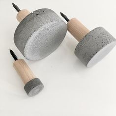 three concrete sculptures with wooden handles and screws on white surface, one is grey and the other is black